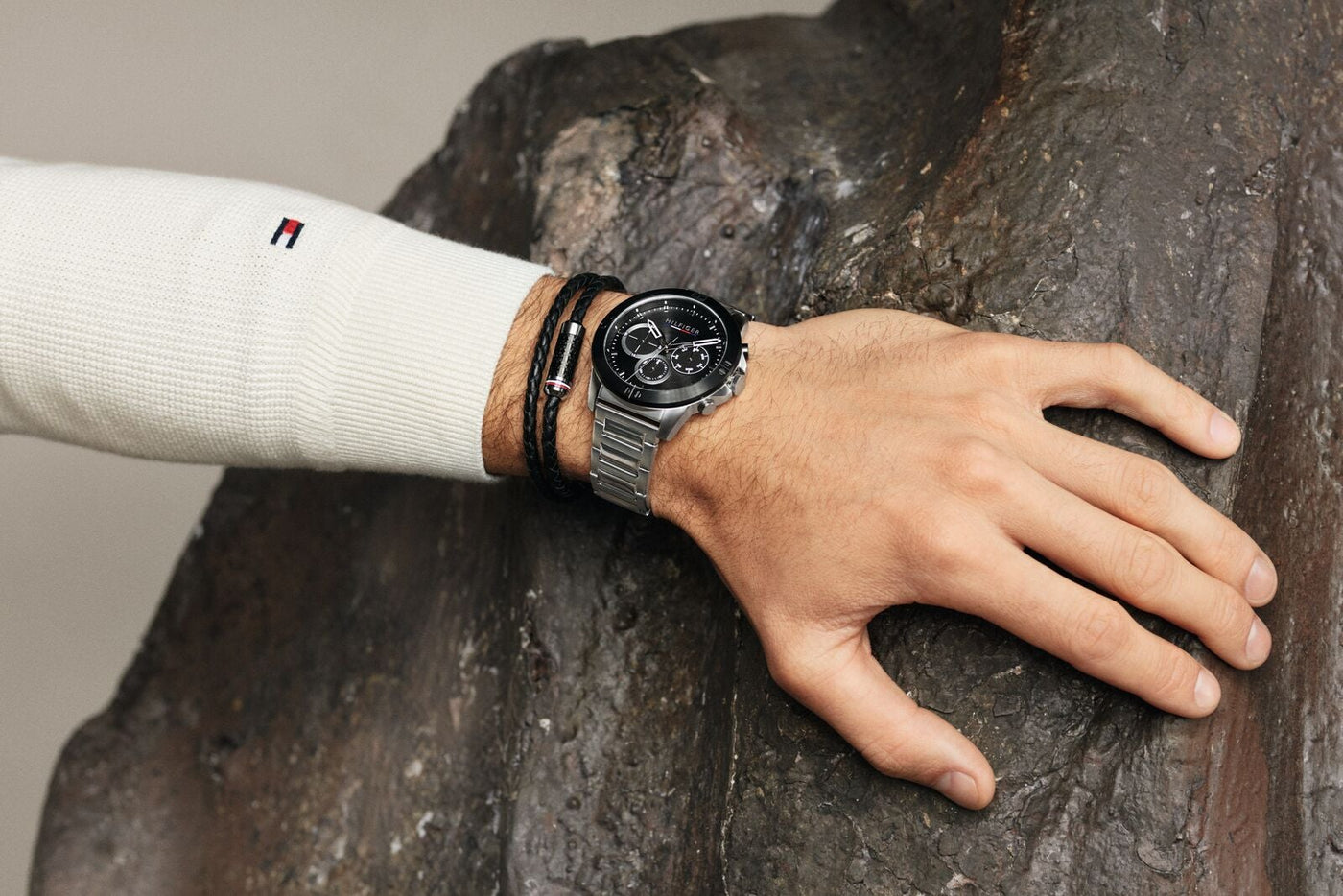 Tommy Hilfiger Men's Watch Dark Grey with Black Face on male models wrist placed on rock.